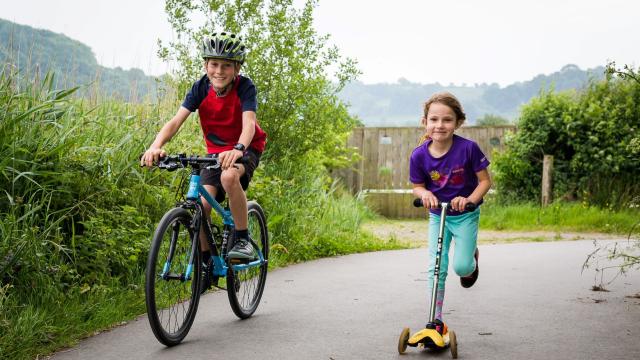 Two children cycle and scoot along a traffic-free route